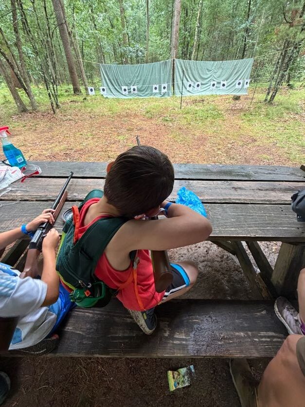 Scout using a handheld device at a wooded campsite picnic table